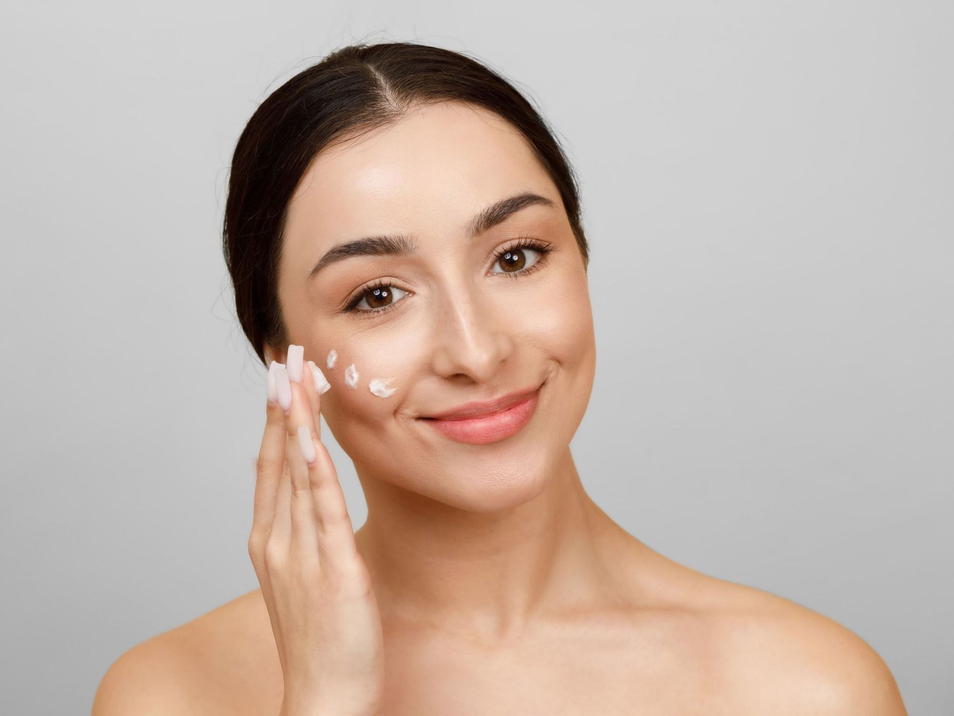 Una mujer sonríe mientras se aplica crema en la cara.