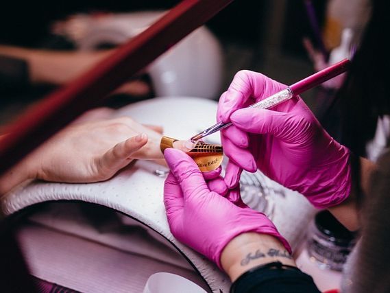 Una persona que lleva guantes rosas está aplicando esmalte de uñas en las uñas de otra persona.