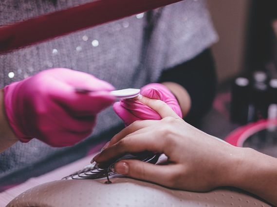 Una mujer se hace las uñas con un técnico de uñas que usa guantes rosas.