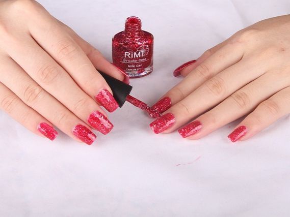Una mujer se aplica esmalte de uñas rojo en las uñas.