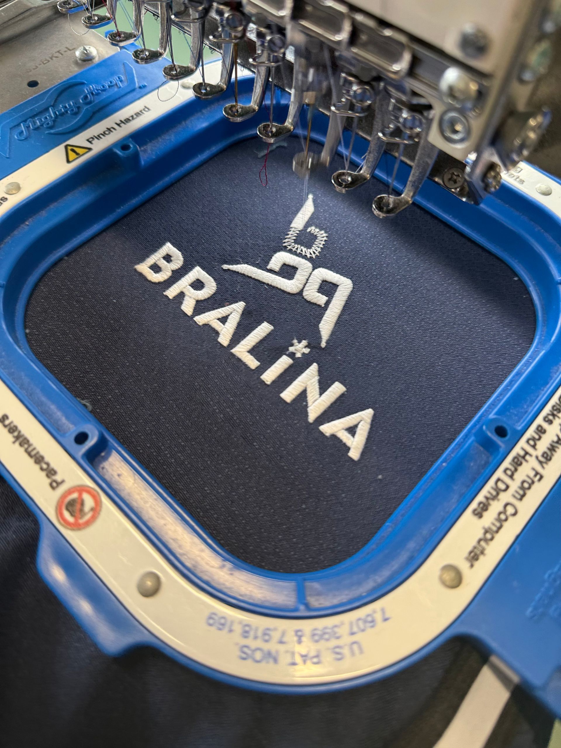 Broderie machine avec logo Brawina blanc sur un cercle à broder bleu foncé