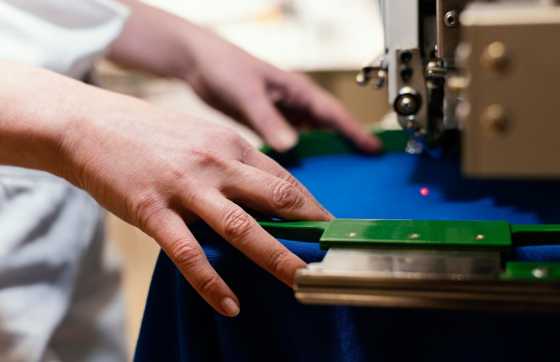 Des mains guident un tissu vert sous une machine à coudre sur une table de travail bleue