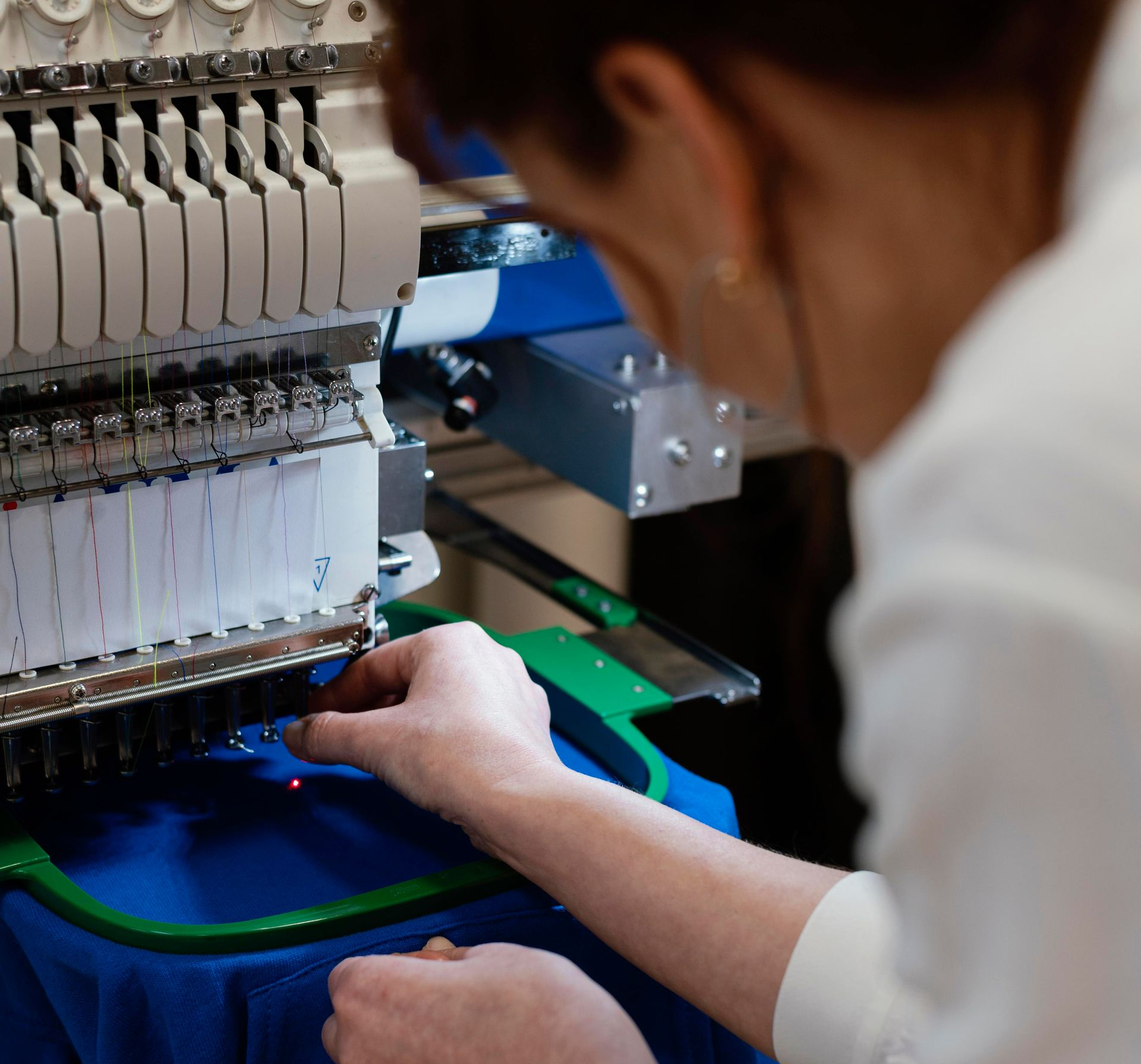 Technicien manipulant une machine à broder sur un cercle à broder bleu dans un atelier