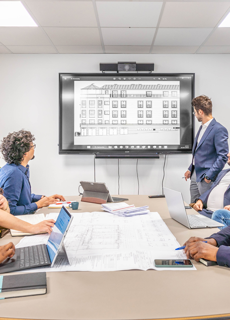 Plusieurs personnes dans un bureau autour d'une table regardant un écran accroché au mur