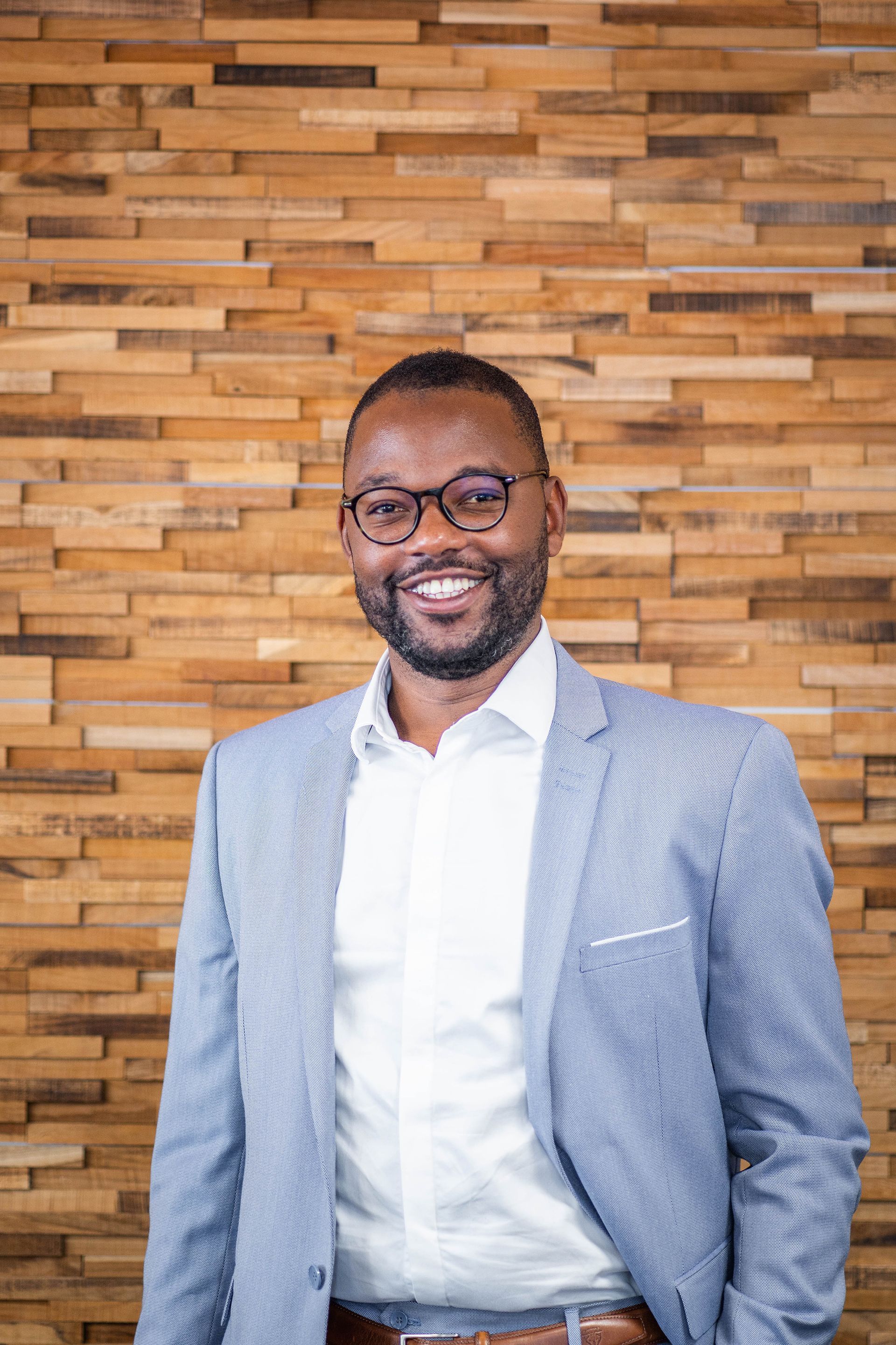 Homme très souriant portant des lunettes et sa main gauche dans la poche