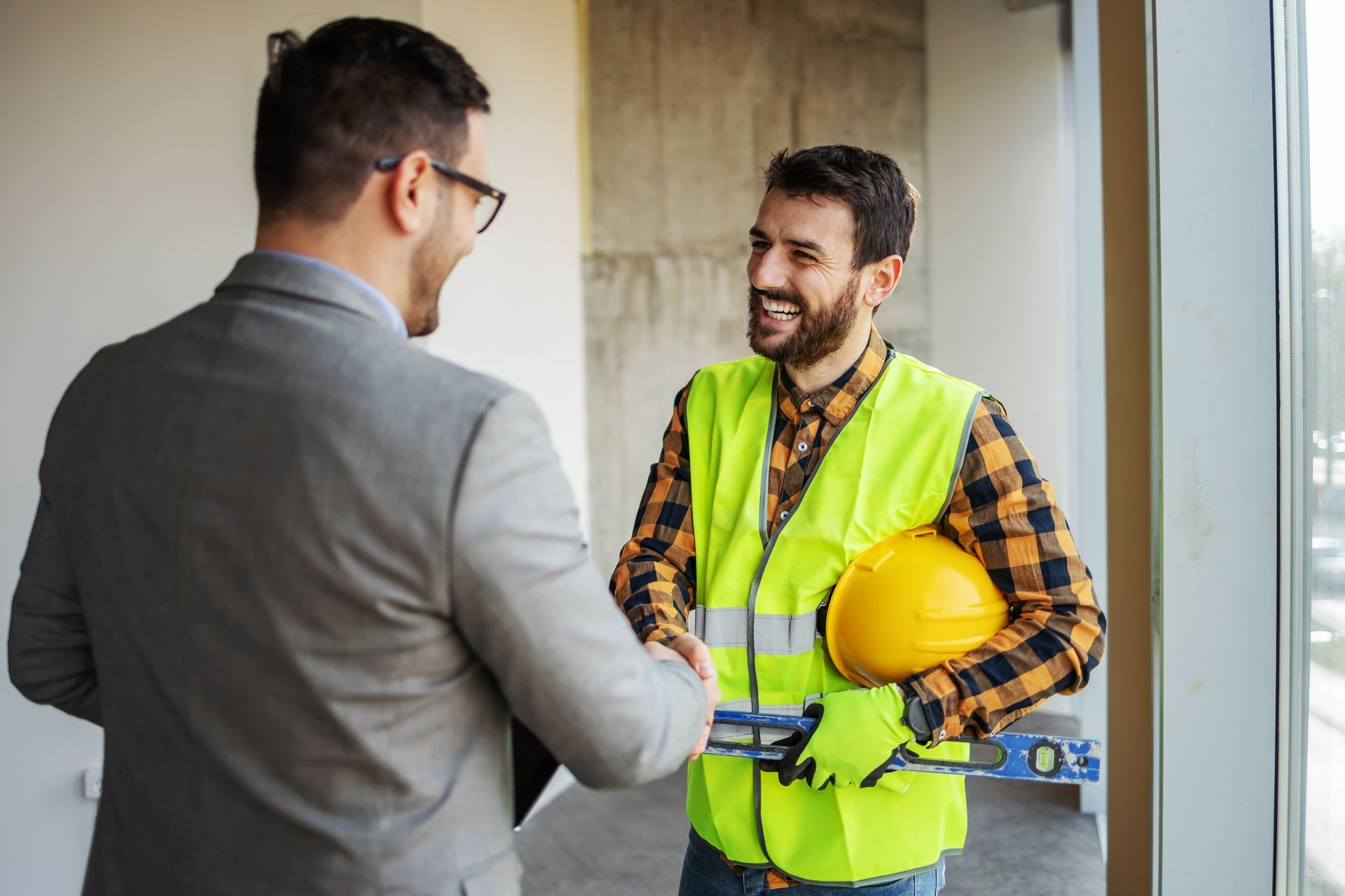 Un ouvrier sur chantier souriant serrant la main d'un homme en costard