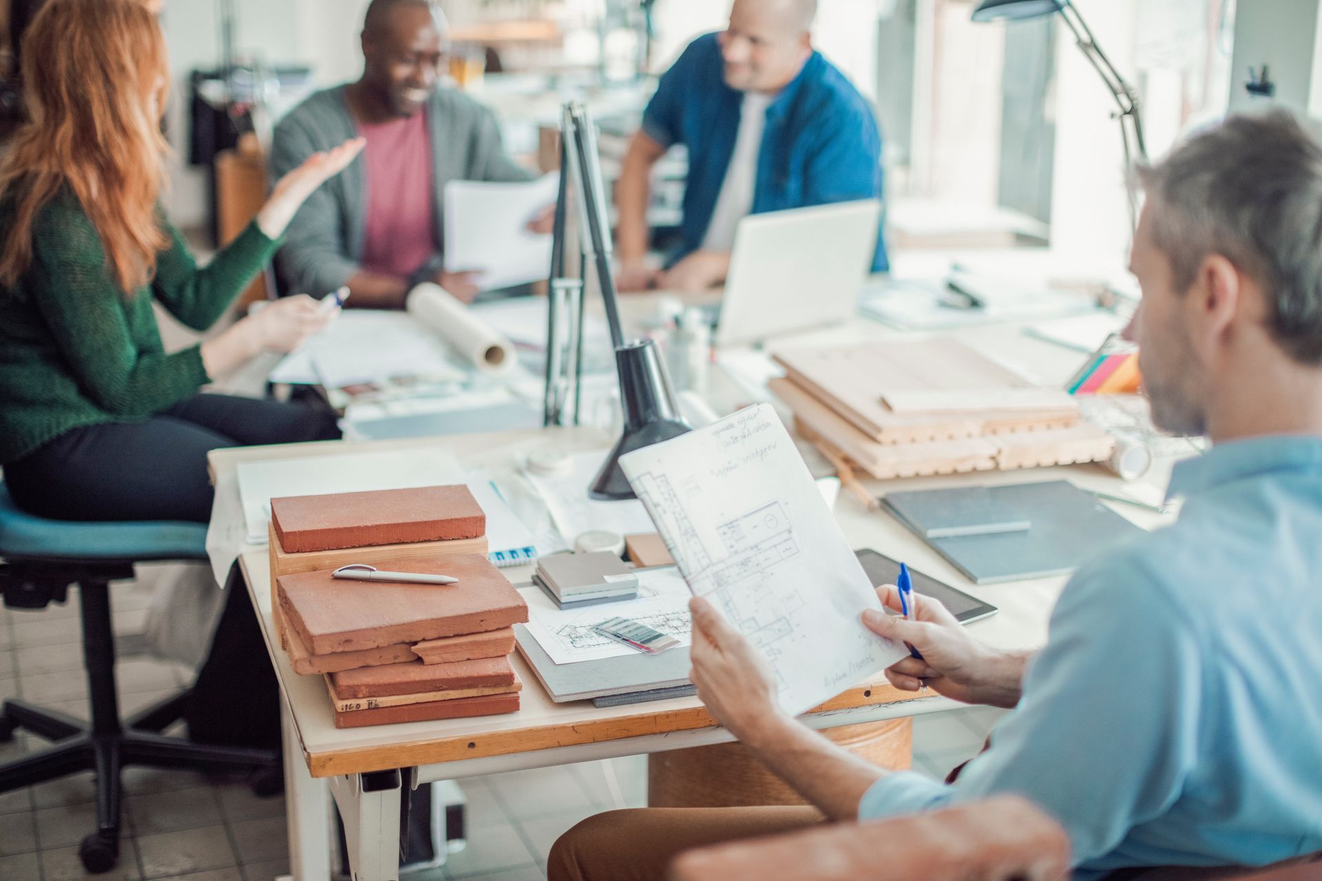 Un homme assis en réunion en train de lire des plans devant une table remplie de matériaux