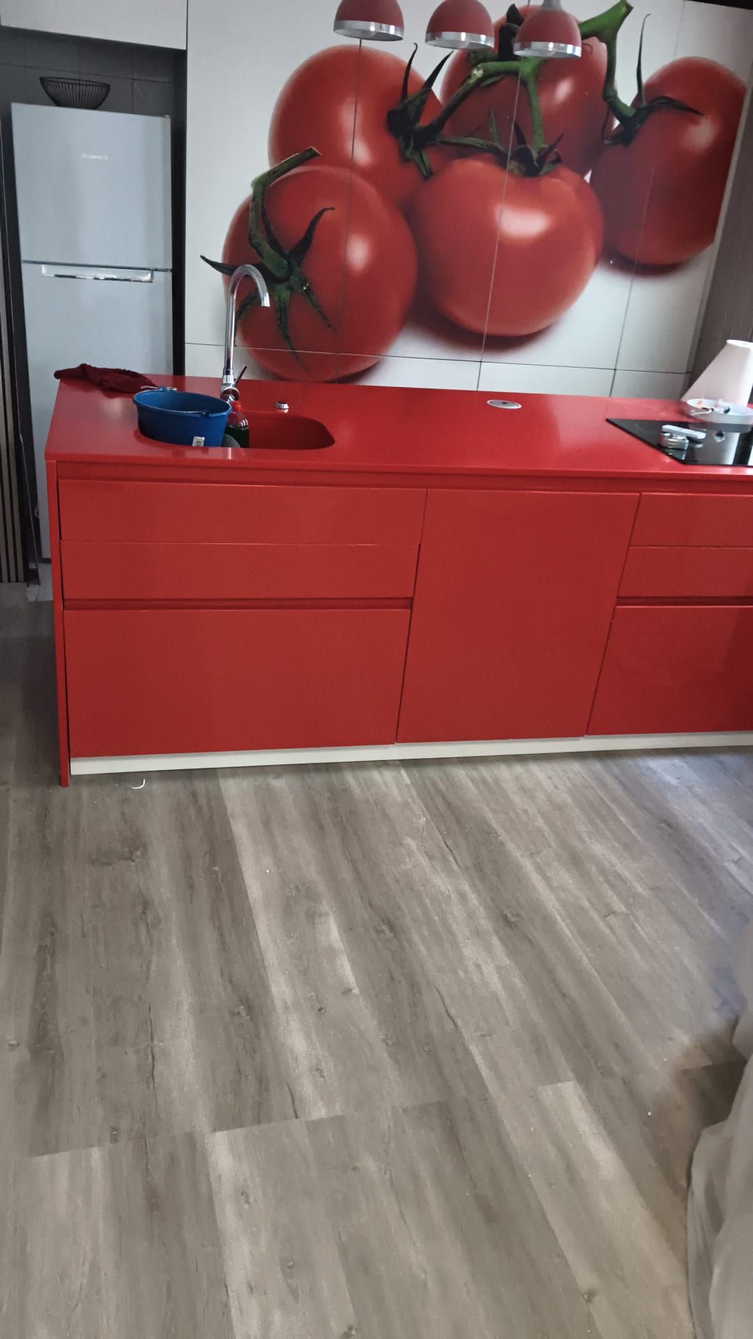 Encimera de cocina roja con mural de tomates, suelo gris y nevera blanca a la izquierda.