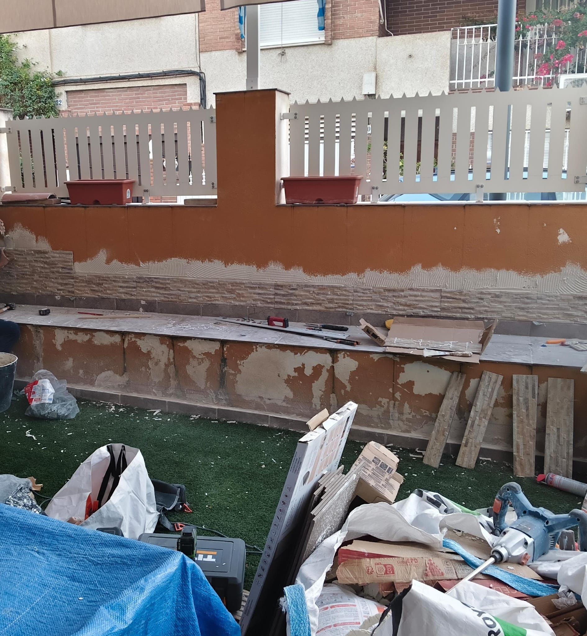 Muro parcialmente demolido con capas expuestas, montones de escombros y una valla blanca encima.