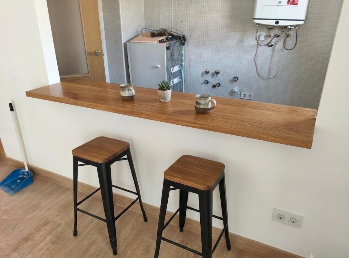 Pequeña encimera de cocina con dos taburetes, mininevera, tazas