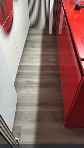 Pasillo estrecho con suelo de madera gris, paredes blancas y armarios o paneles de color rojo brillante a la derecha.