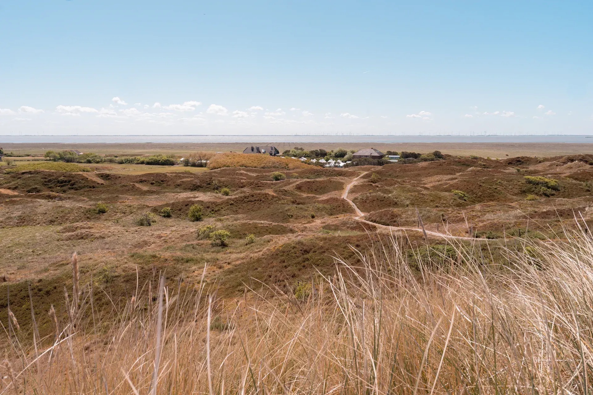 Sandstrand mit glitzerndem Wasser, Ebbe und einem entfernten, linearen Bauwerk.
