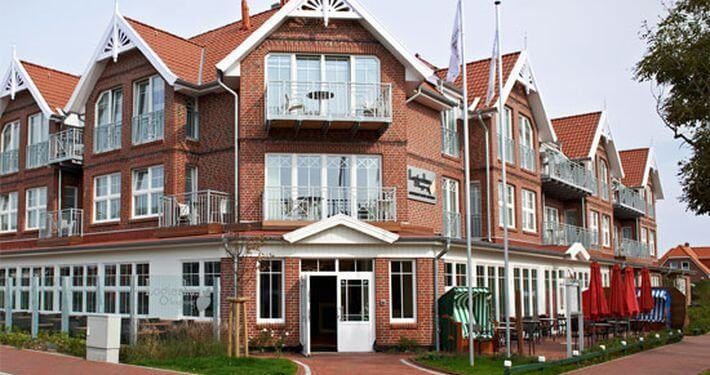 Mehrstöckiges Hotel aus rotem Backstein mit weißen Zierelementen, Balkonen und einem Sitzbereich im Freien.