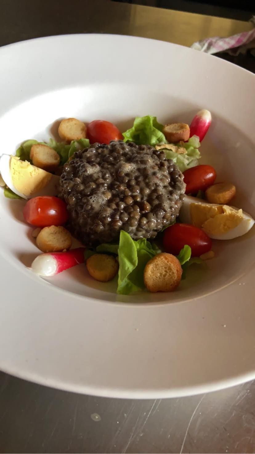 Salade de lentilles, tomates, radis, croûtons et œuf sur une assiette blanche.