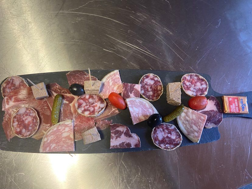 Planche de charcuterie avec viandes séchées, cornichons, olives et tomates, présentée sur un plateau en ardoise.