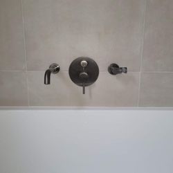 Paroi de douche avec baignoire, robinetterie chromée et carrelage beige.