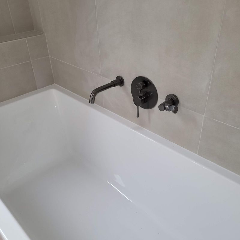 Baignoire blanche avec mur carrelé beige et robinetterie chromée dans une salle de bains.