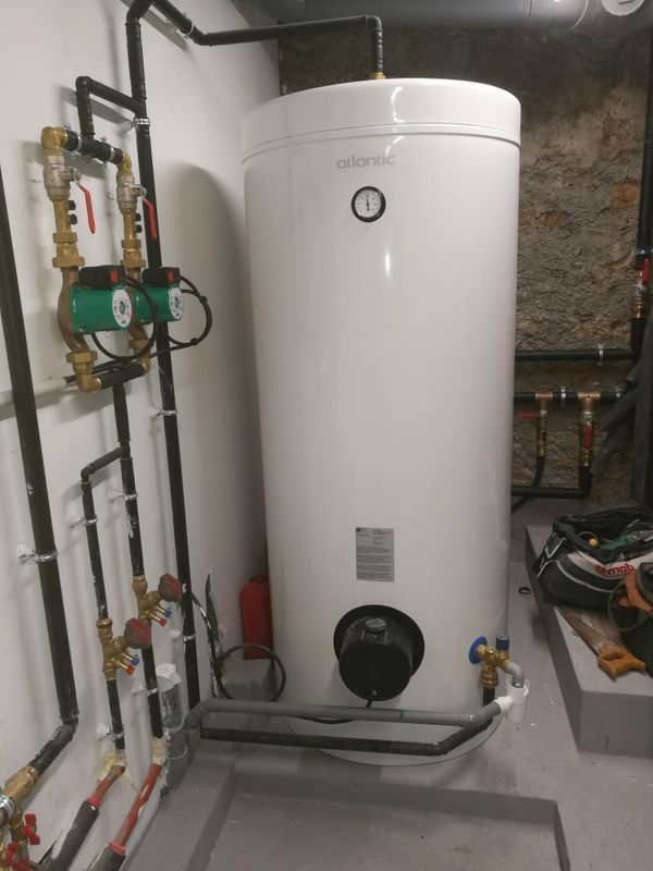 Chauffe-eau cylindrique blanc avec tuyaux et vannes dans une buanderie au sous-sol.