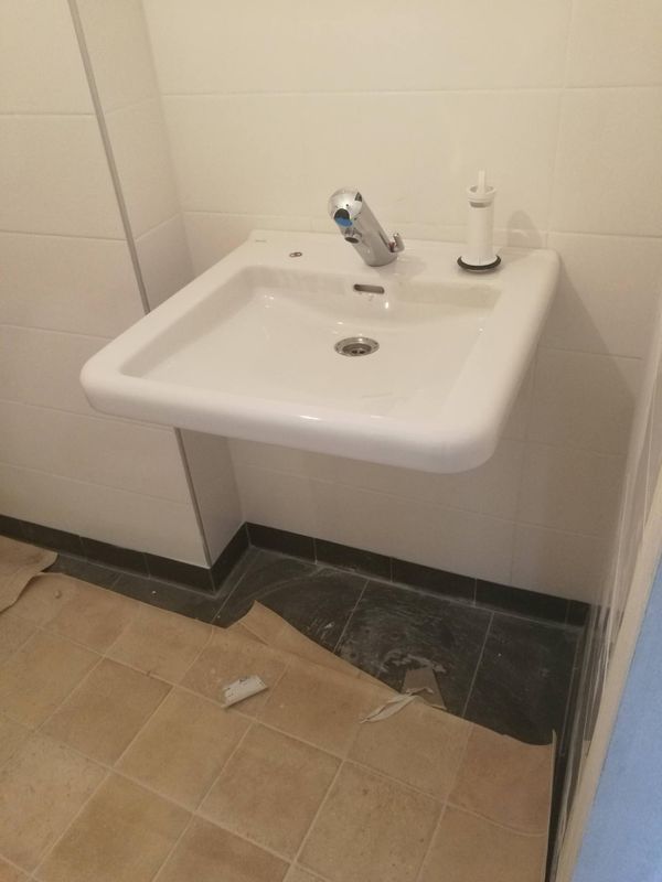 Lavabo blanc mural avec robinet chromé dans un coin carrelé de salle de bains.