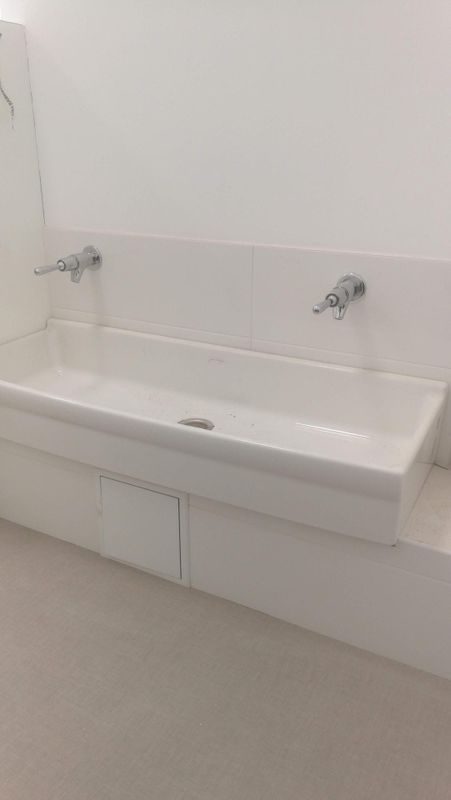 Lavabo de salle de bain blanc avec deux robinets muraux et crédence carrelée contre un mur uni.