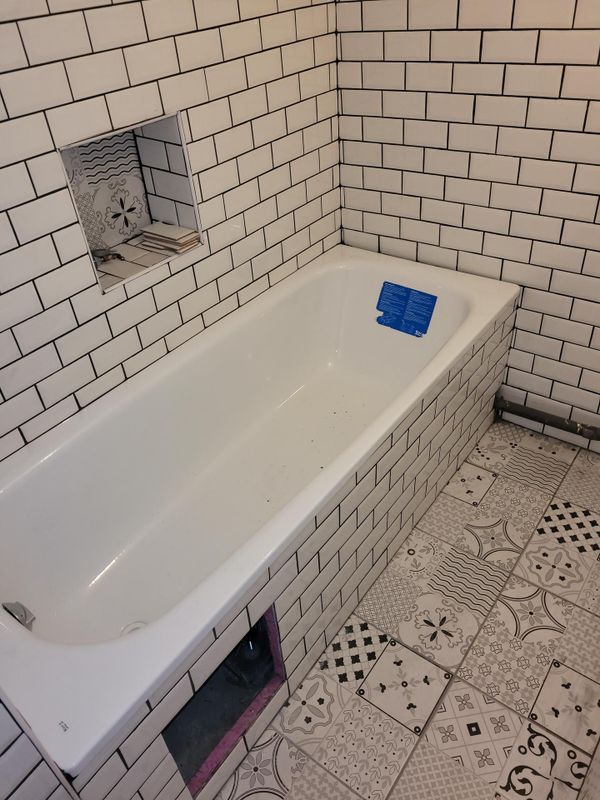 Salle de bains avec baignoire blanche, murs et sol carrelés, et un objet bleu sur le rebord de la baignoire.
