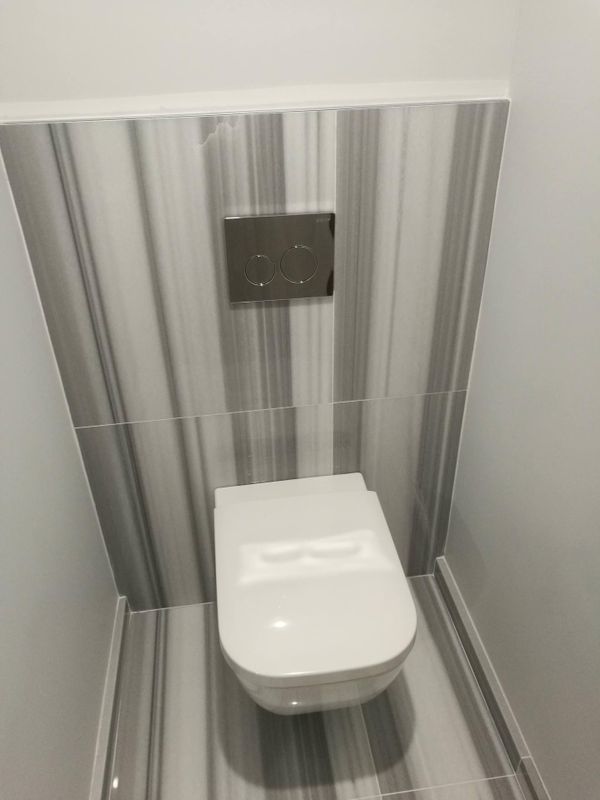 Petite cabine de toilettes avec cuvette mural blanc et panneaux à rayures grises.