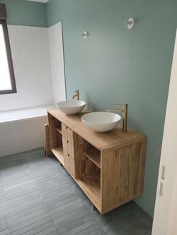 Salle de bains moderne avec murs vert menthe, deux vasques blanches et un meuble sous lavabo en bois près d'une fenêtre.