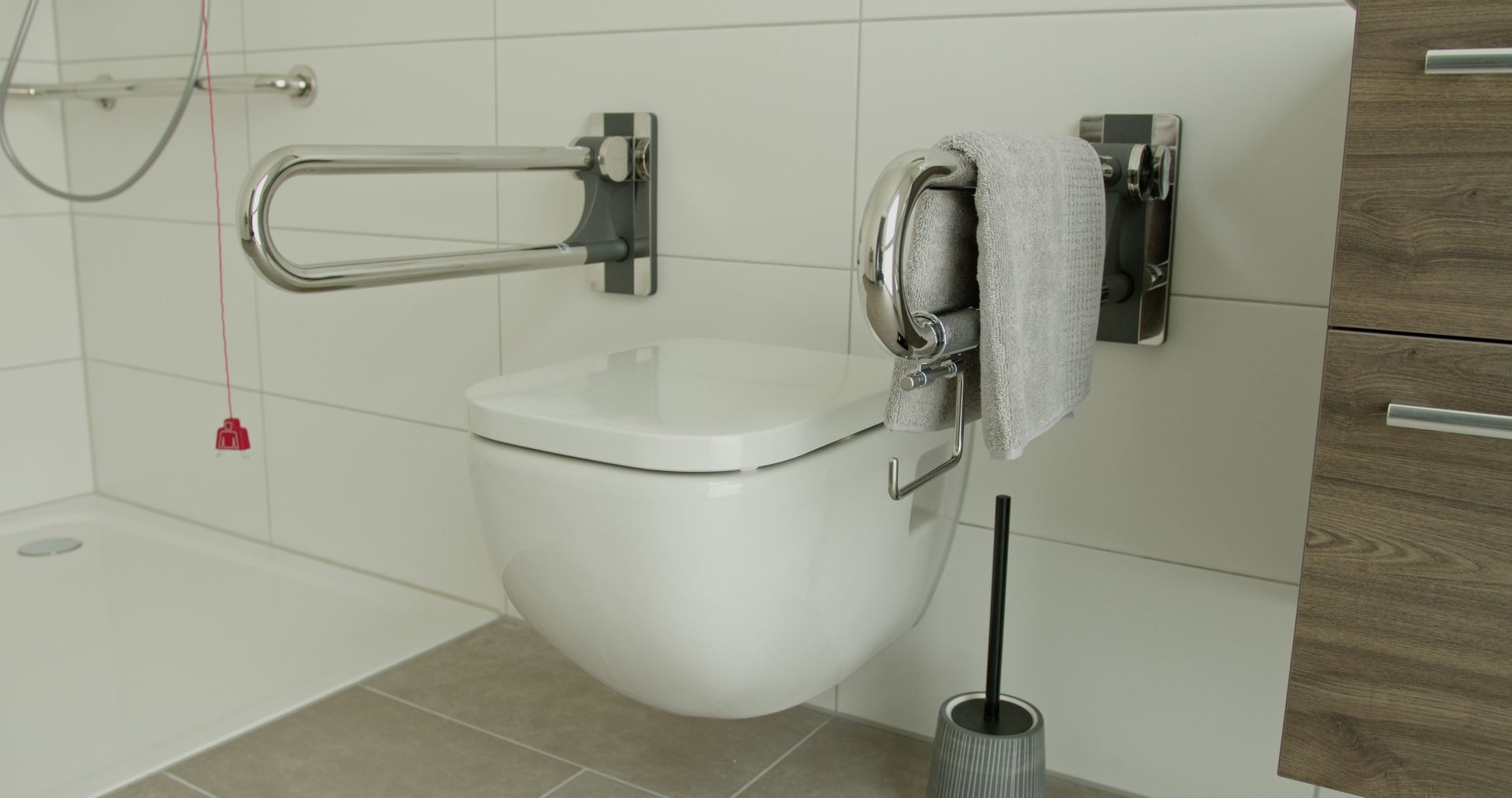 Salle de bains accessible avec toilettes suspendues, barre d'appui et porte-papier toilette.