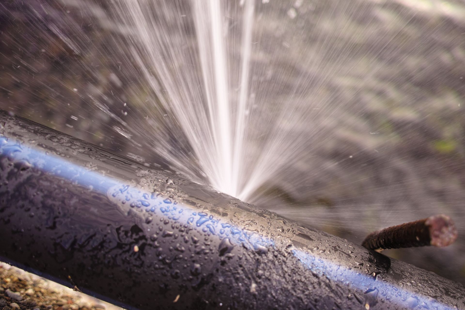 De l'eau jaillissant d'un tuyau sur une surface métallique sombre, créant des éclaboussures et des gouttelettes brillantes.