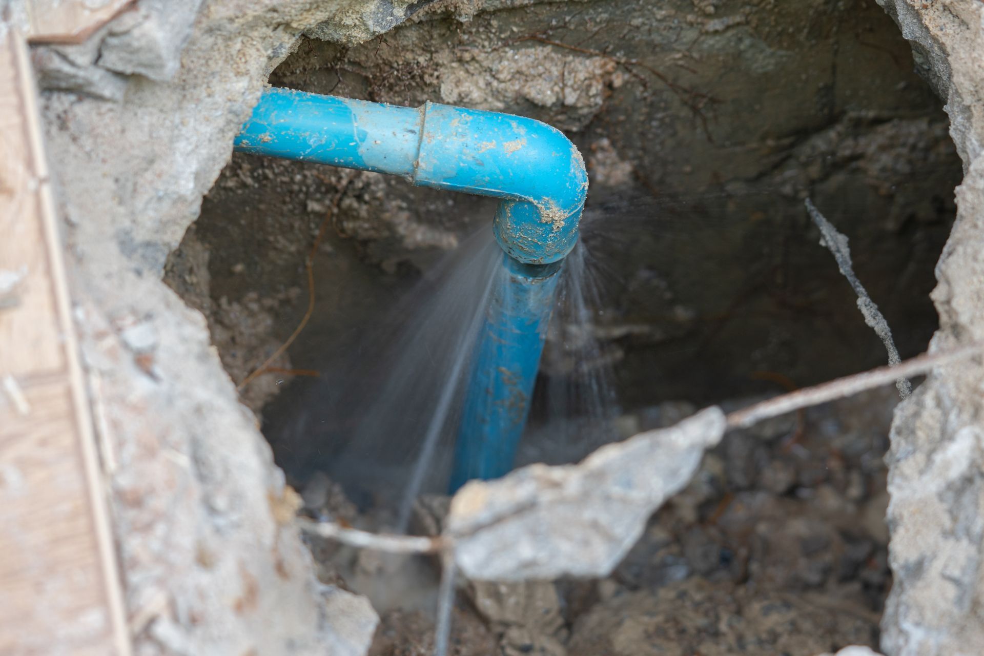 Un tuyau en PVC bleu fuit de l'eau dans une fosse à terre à travers une ouverture dans le sol.