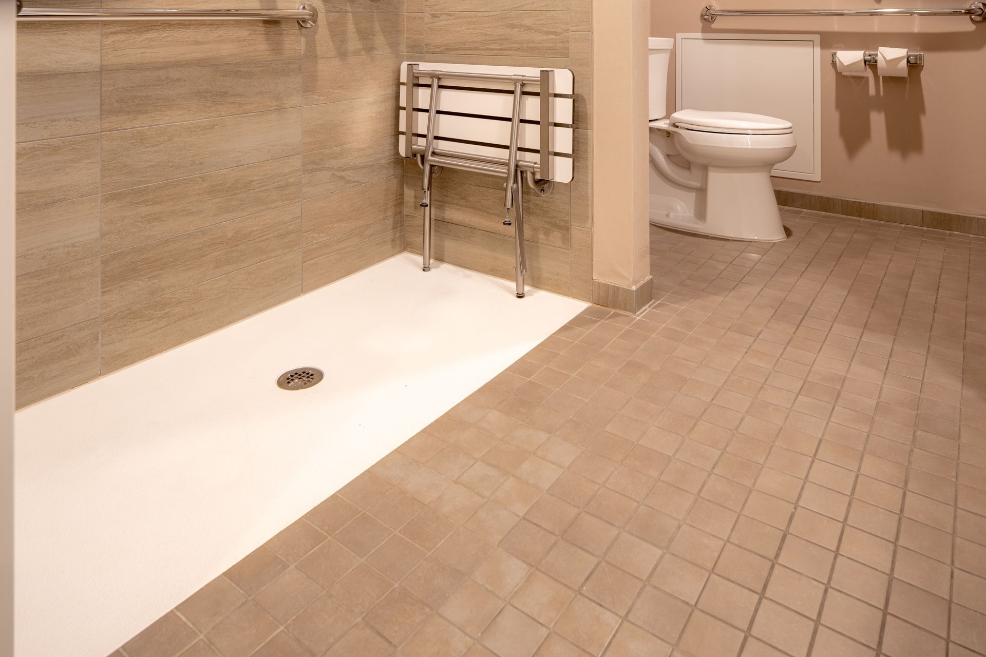 Salle de bains accessible avec douche à l'italienne, siège de douche, toilettes et carrelage beige au sol.