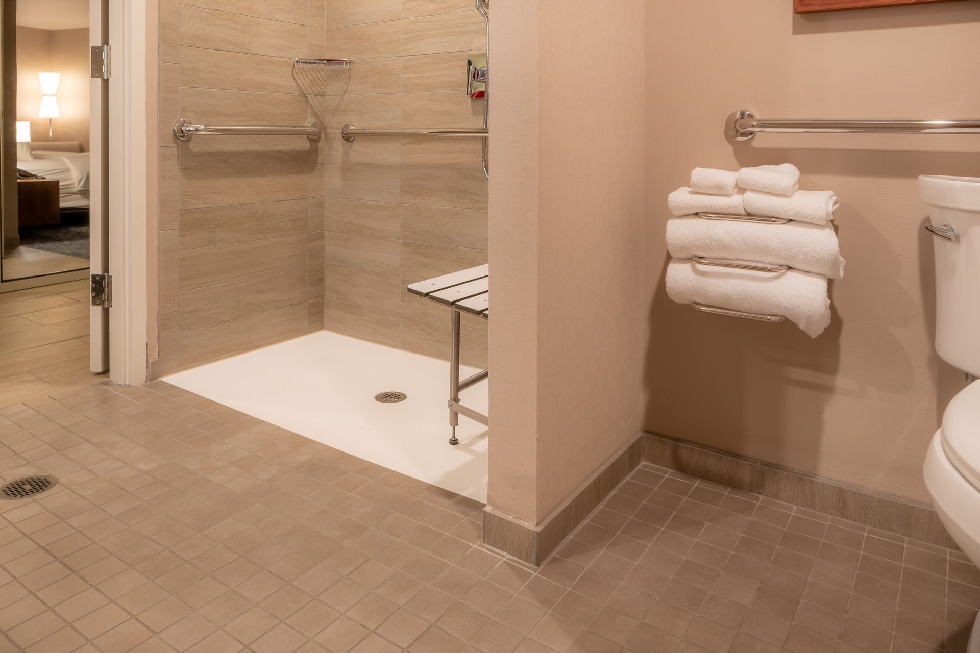 Salle de bain d'hôtel accessible avec douche à l'italienne, sol carrelé et porte-serviettes mural.