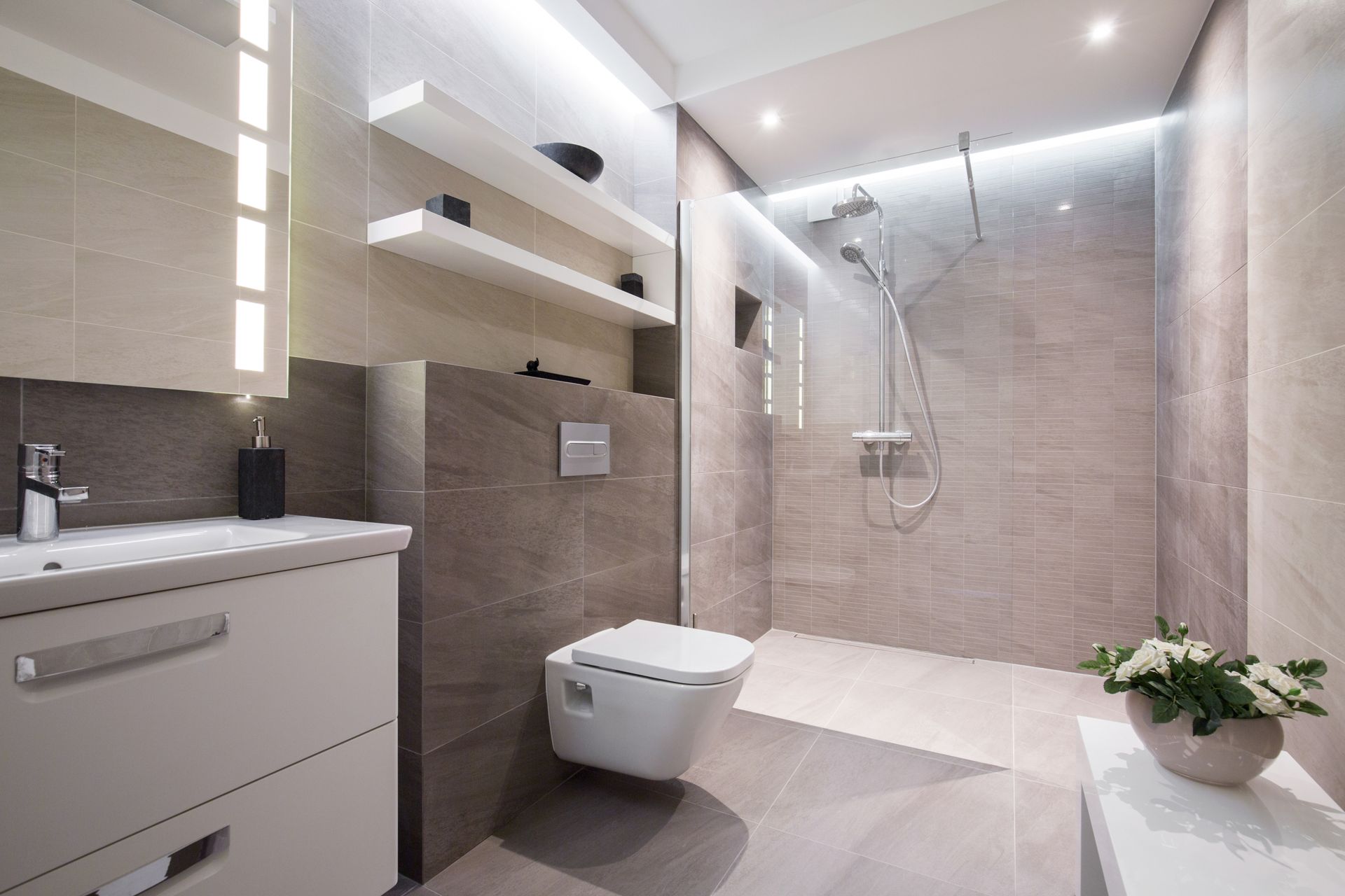 Salle de bains moderne beige avec douche à l'italienne, WC suspendus, meuble sous lavabo et plante en pot.