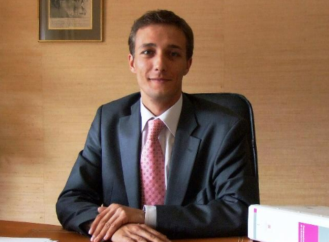 Un homme en costume signe des documents à un bureau, en présence de la balance de la justice et d'un marteau de juge.