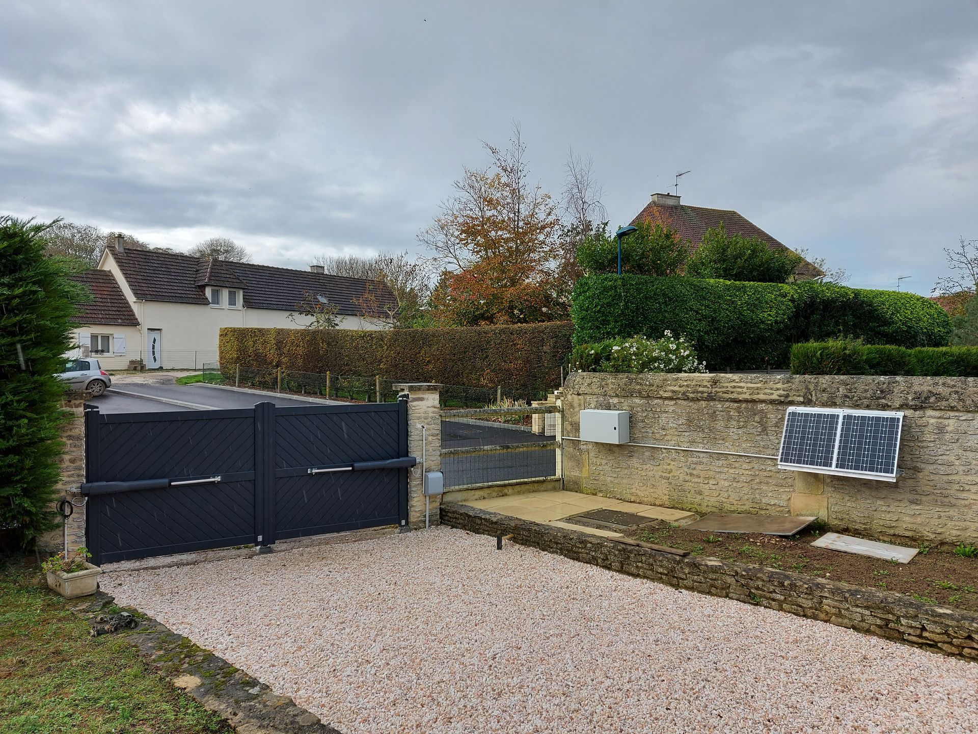 Une allée avec une clôture et un portail battant avec bras articulé