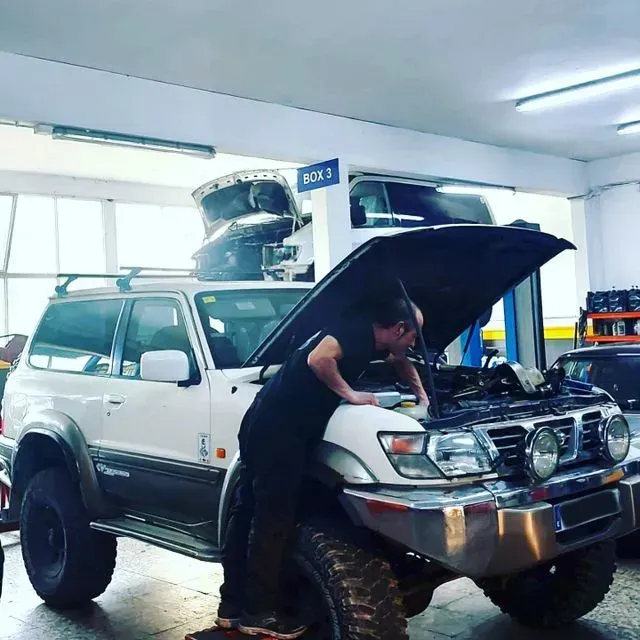 Un hombre está trabajando en una camioneta blanca con el capó abierto.
