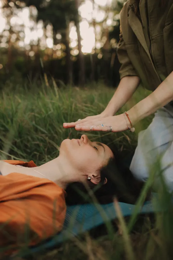 Manos sobre la cabeza de una persona al aire libre, en una postura de curación o meditación.