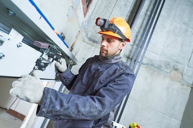 Ein Mann mit Schutzhelm und Handschuhen arbeitet an einem Aufzug.