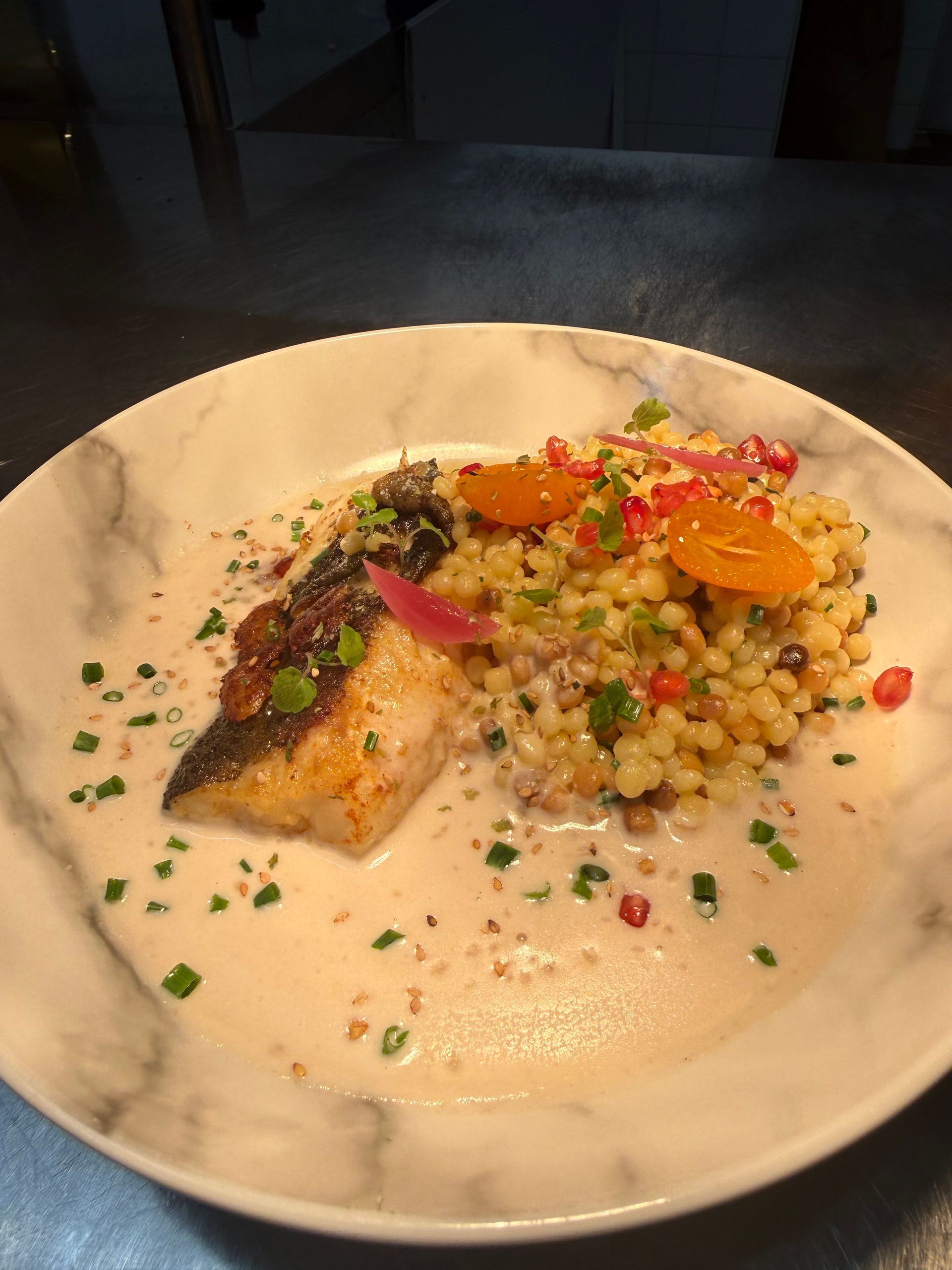 Poisson poêlé avec couscous, tranches d'orange et sauce sur une assiette marbrée.