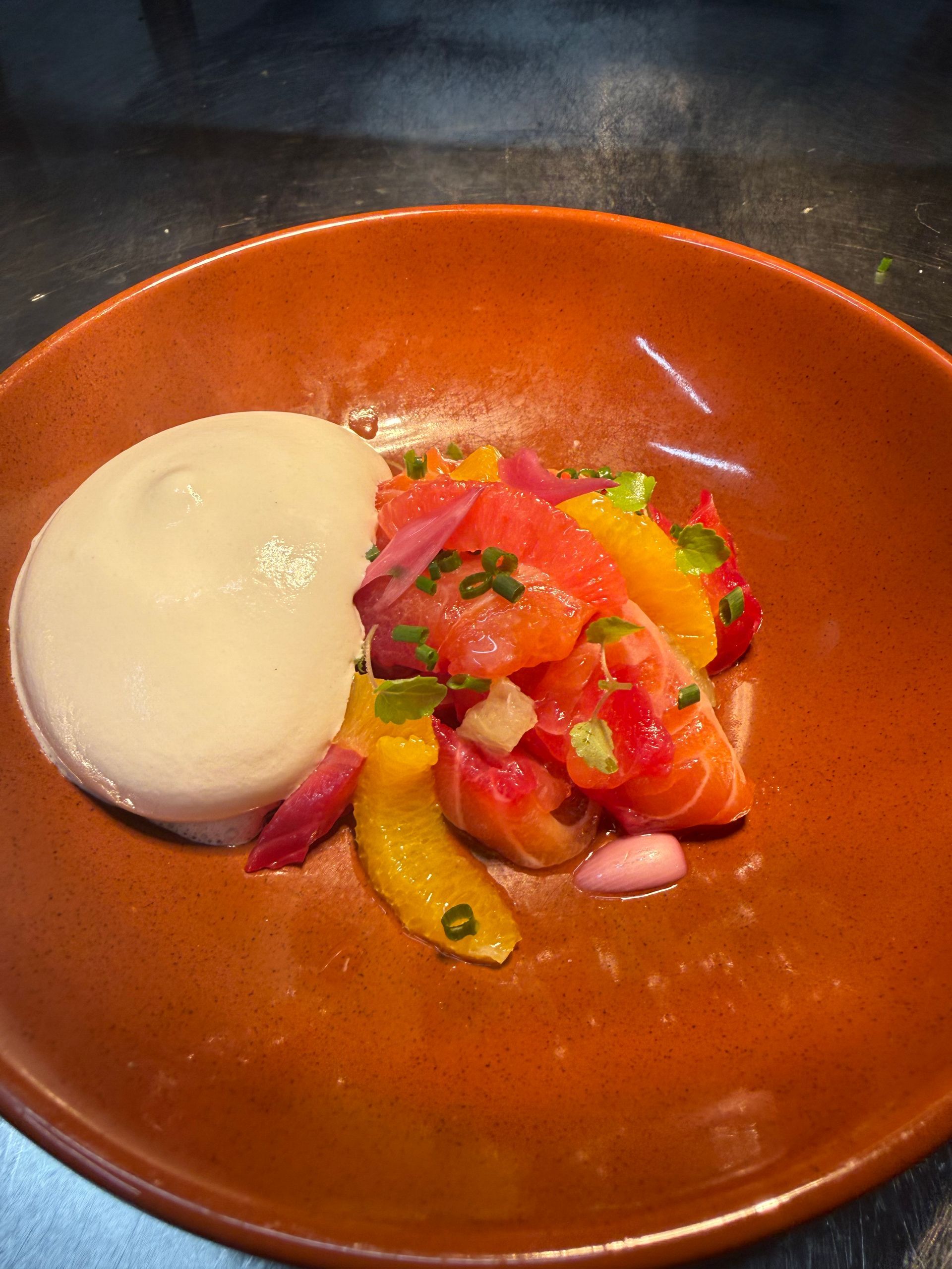 Assiette orange avec une cuillerée blanche à côté d'agrumes hachés et d'oignons rouges.