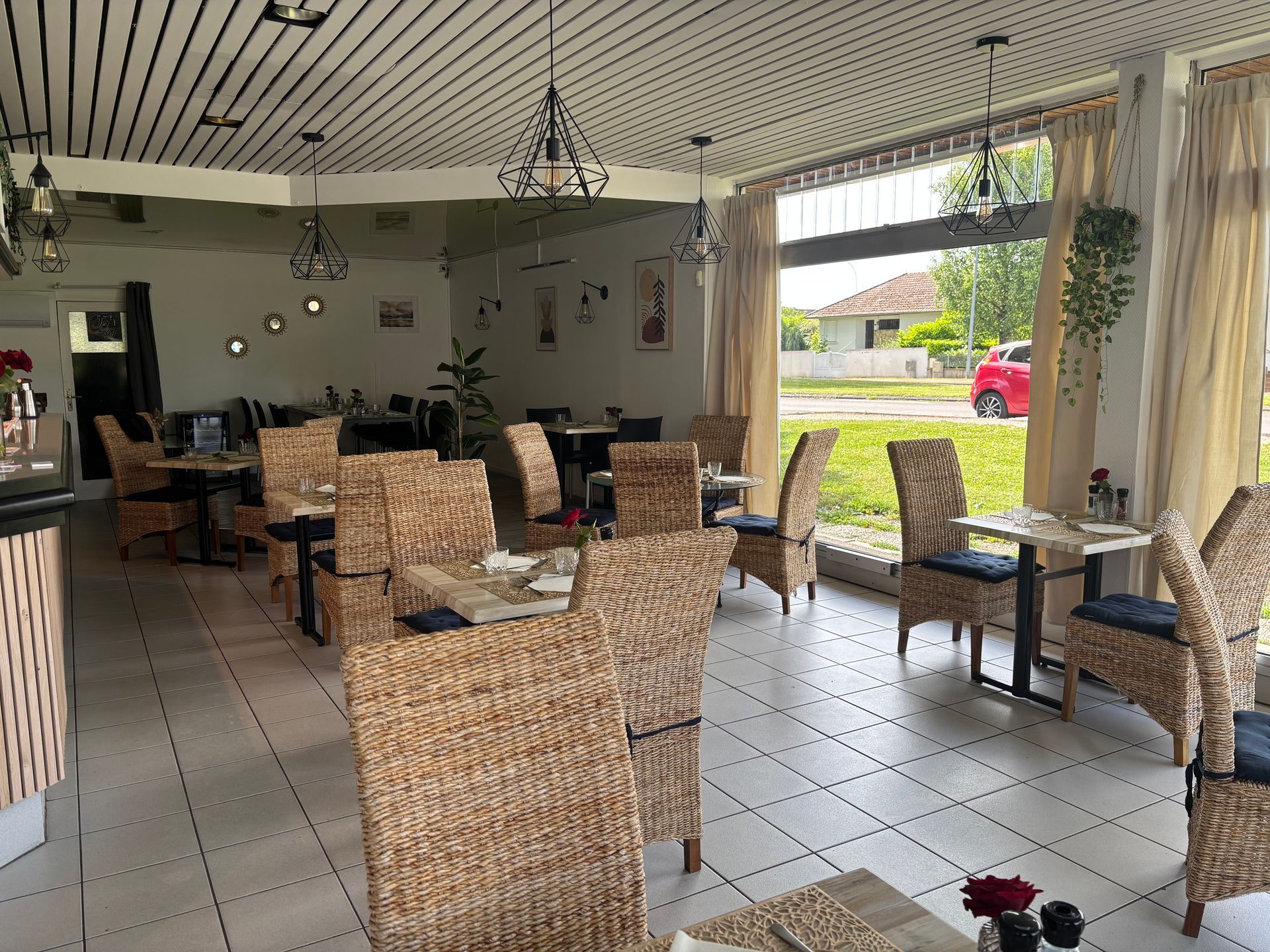 Vue intérieure du restaurant L'ENVIE avec des chaises tissées, des tables et de grandes fenêtres donnant sur une rue.