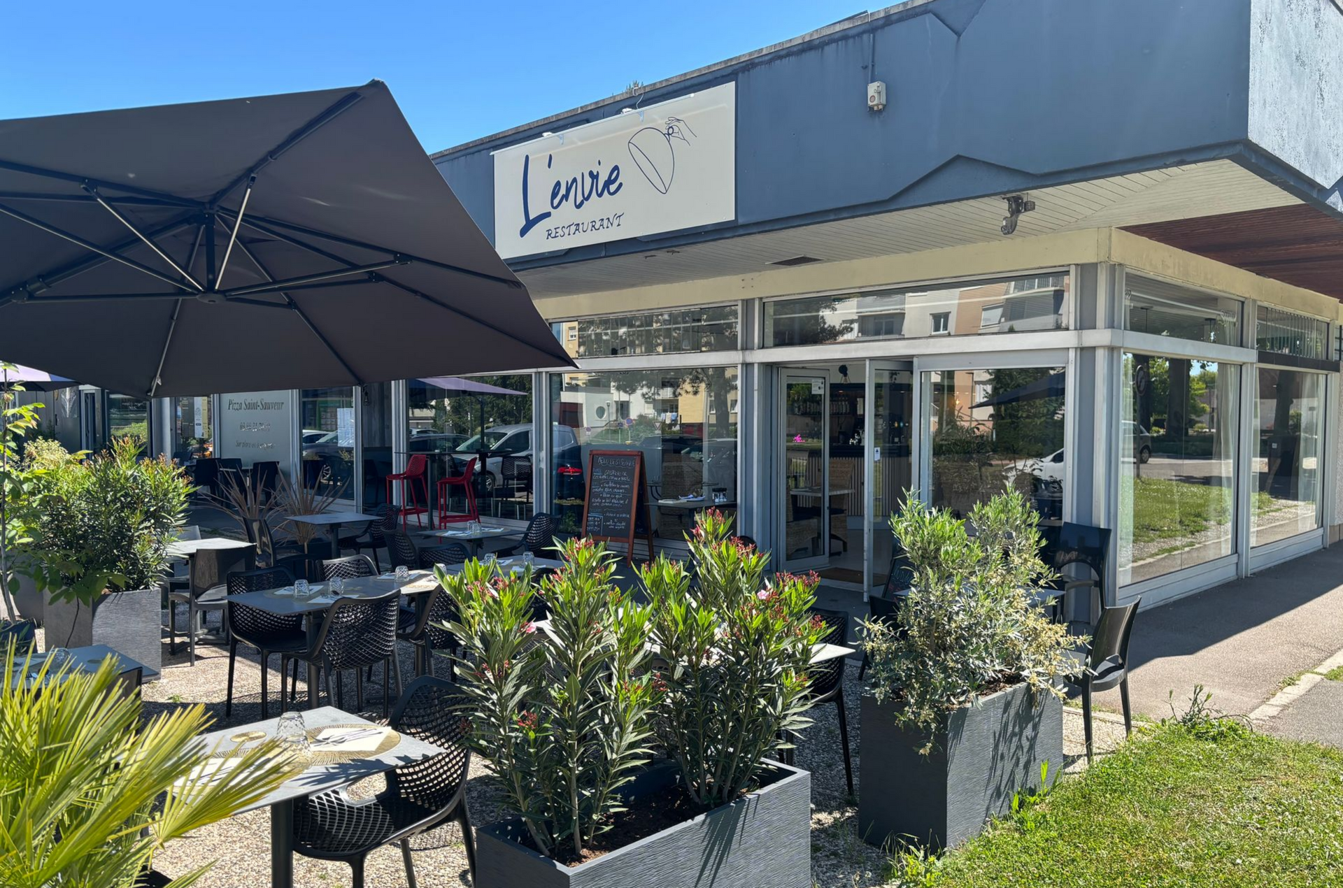 Restaurant L'ENVIE avec terrasse extérieure, plantes et parasol.