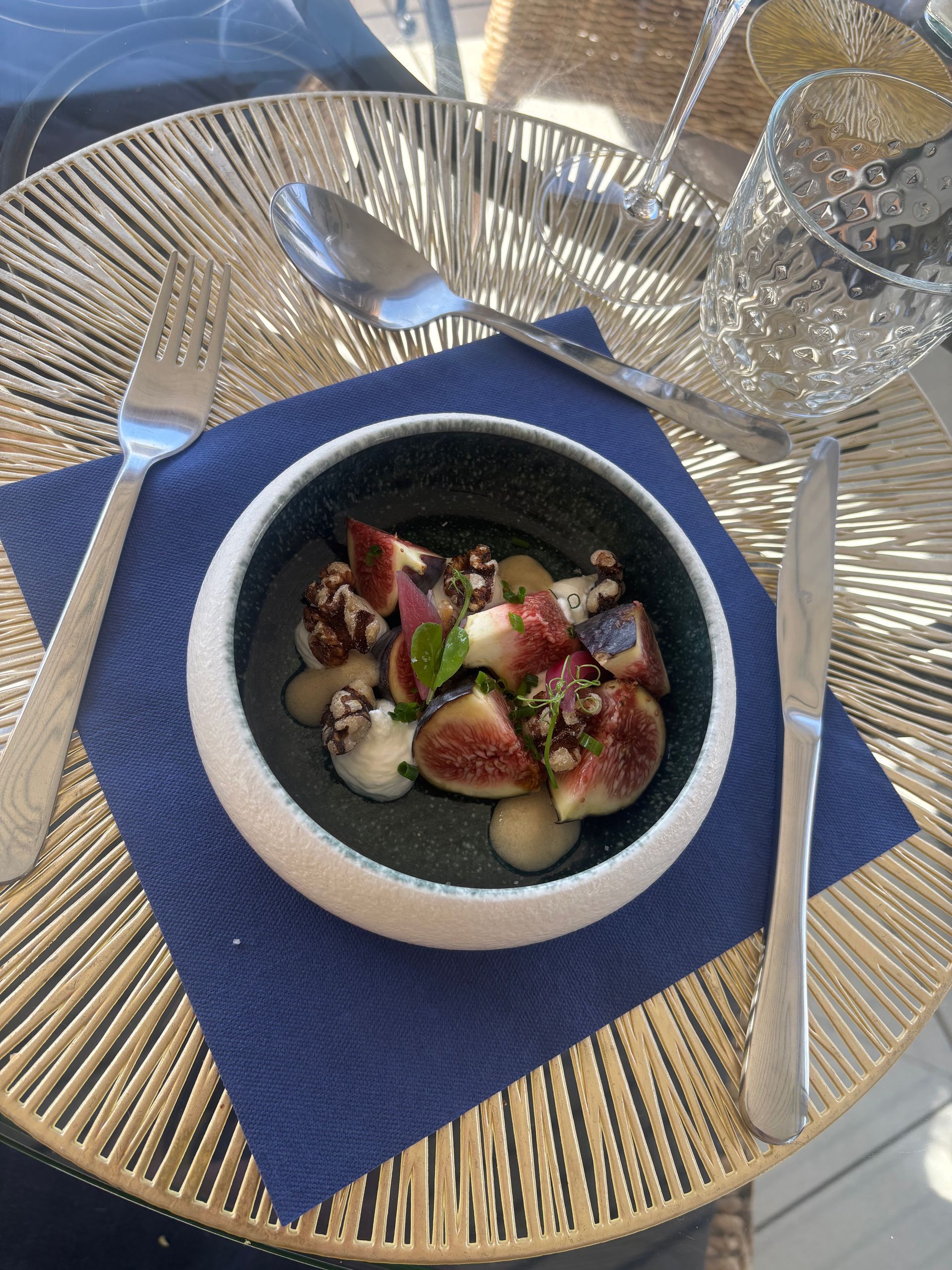 Un bol de figues et de sauce sur une serviette bleue, avec des couverts sur un plat doré.