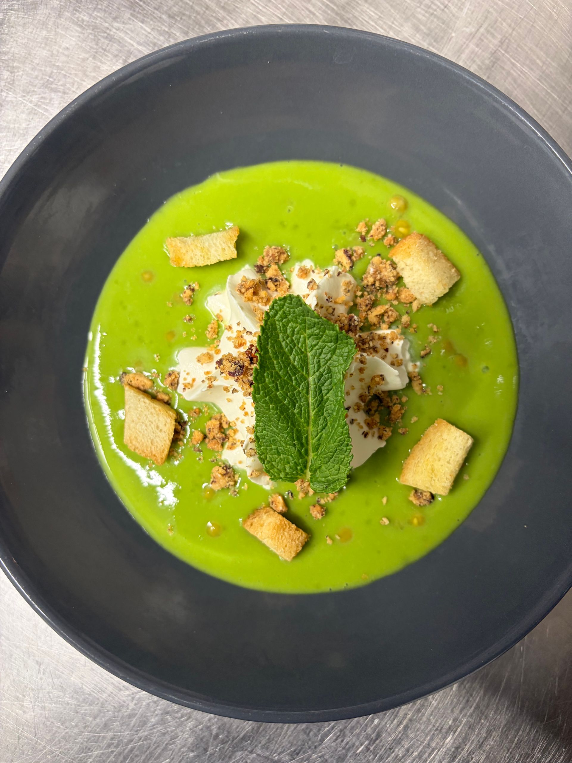 Une salade colorée avec des boules de melon, du jambon et une feuille décorative sur une assiette sombre.