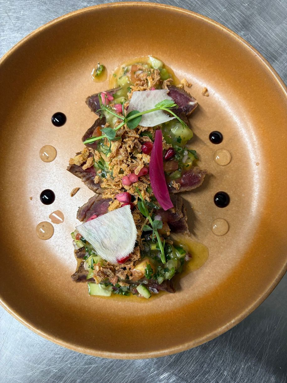 Une salade colorée avec des boules de melon, du jambon et une feuille décorative sur une assiette sombre.