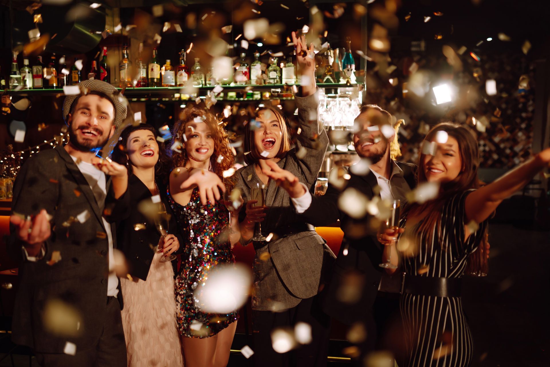 Dans un bar, les gens font la fête, les confettis tombent. Visages souriants, bras levés.