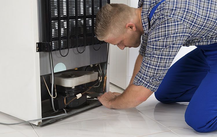 Un hombre se arrodilla para arreglar un refrigerador.