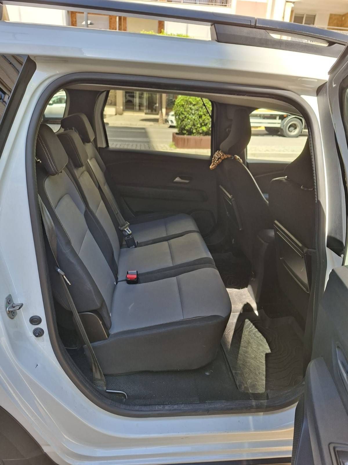 El interior de un vehículo blanco con un asiento trasero corrido de tela gris y puertas del lado del pasajero abiertas.