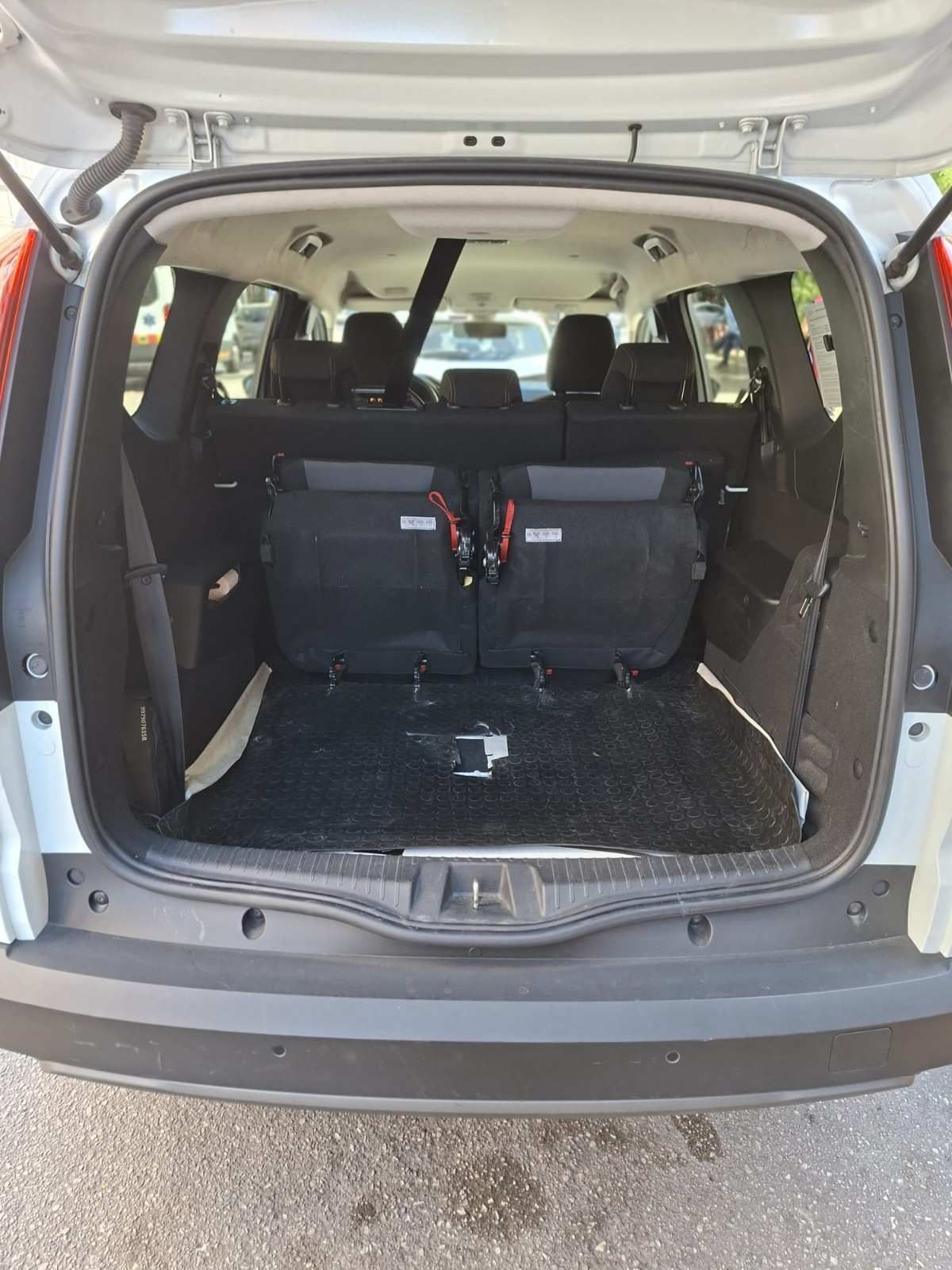 El maletero de un vehículo blanco está abierto, dejando ver una alfombrilla negra y dos asientos traseros abatidos orientados hacia adelante.
