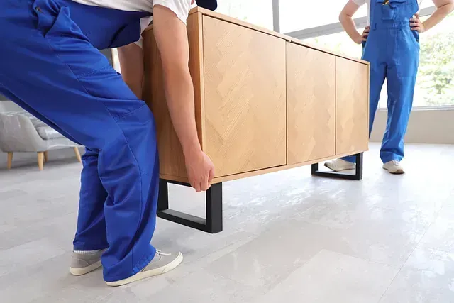 Dos trabajadores transportan un armario de madera en una sala de estar.